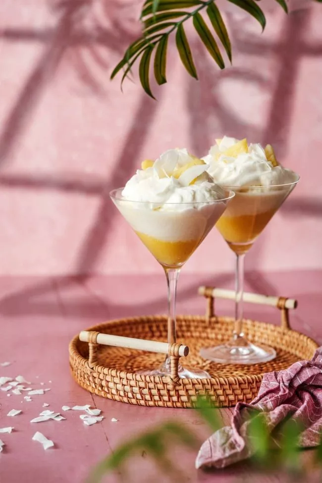 zwei Martini gläser gefüllt mit frischer ananaspüree und einer Mousse aus Batida de coco und sahne.