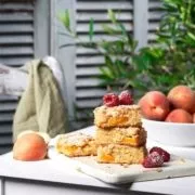 Pfirsichkuchen angerichtet auf einem weißen Tisch mit Pfirsichen im Hintergrund